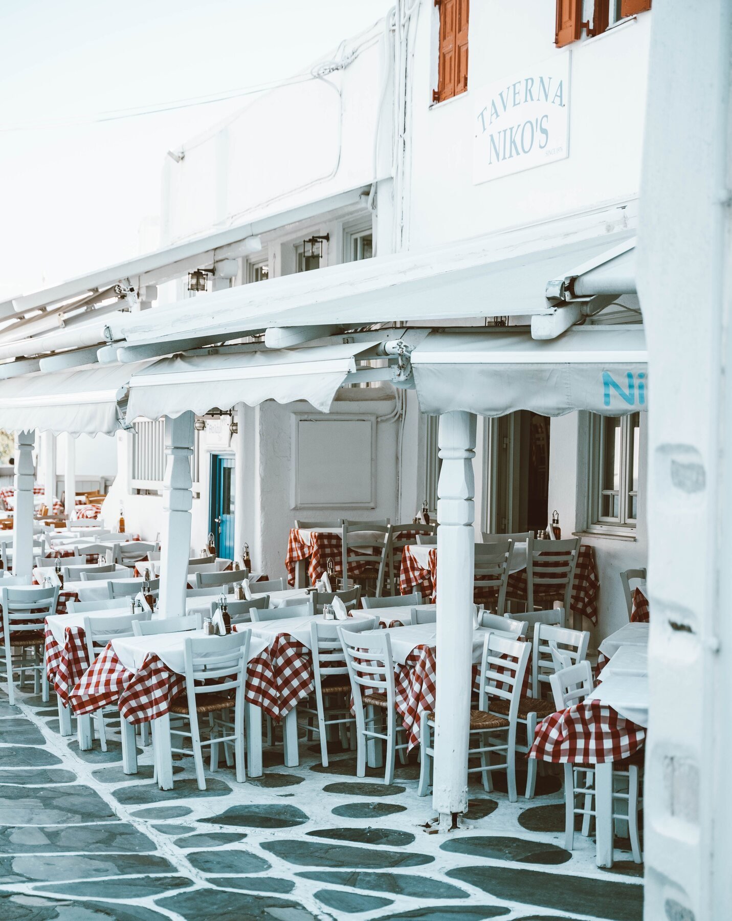 Small traditional Greek taverna with white chairs and checked tablecloths